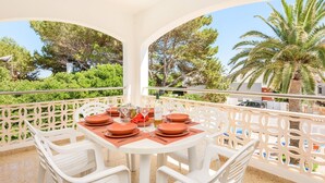 A dining area with a table set for four, surrounded by white chairs, overlooking a scenic view of trees and a palm tree. - Villa Imogen by Villa Plus (Cap d'Artrutx)