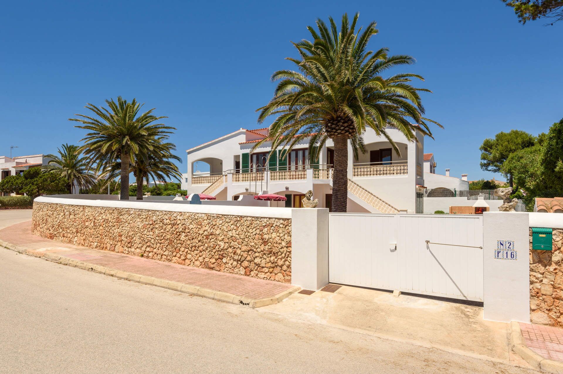 A modern two-story house with a stone wall, a balcony, and a palm tree.
