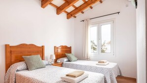 Ein Schlafzimmer mit zwei Betten, Holzkopfteilen, einem Fenster mit Vorhängen und einer Holzbalkendecke.