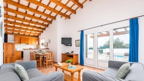Ein geräumiges Wohnzimmer mit hoher Decke, einem Essbereich und Blick auf einen Swimmingpool durch große Glasüren.