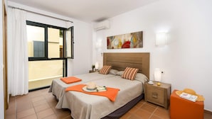 Una habitación de hotel con cama, mesita de noche, lámpara, ventana con cortinas y un cuadro en la pared.