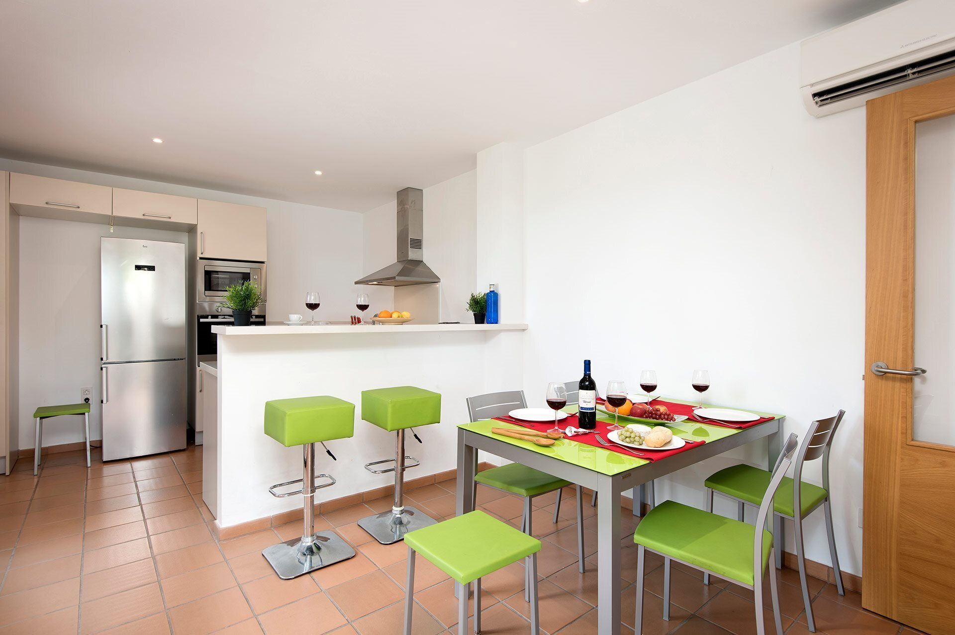 Una cocina moderna con refrigerador empotrado, una mesa de comedor con sillas y una puerta de madera.