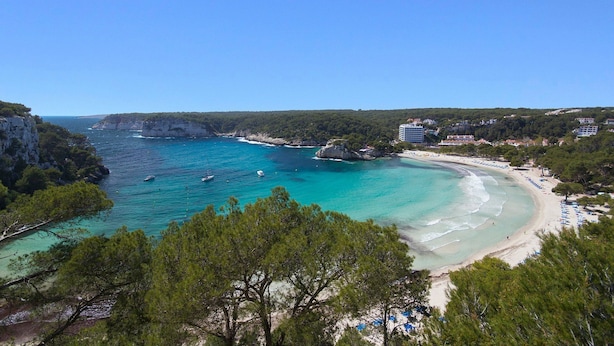 Vista costera con aguas turquesas cristalinas, una playa arenosa y una zona boscosa.