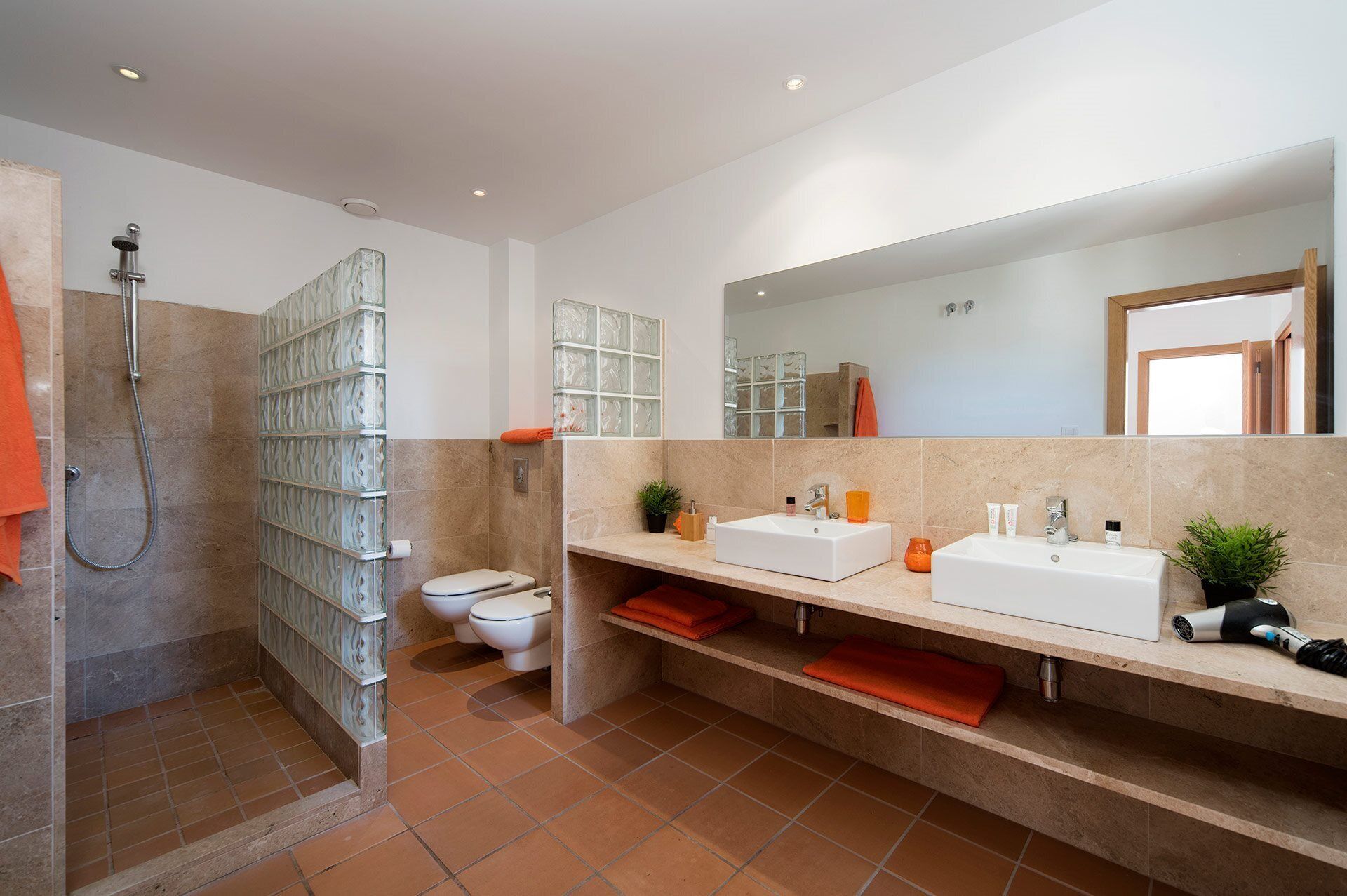Un baño moderno con cabina de ducha de vidrio, inodoro, espejo grande y tocador con dos lavamanos y encimera.