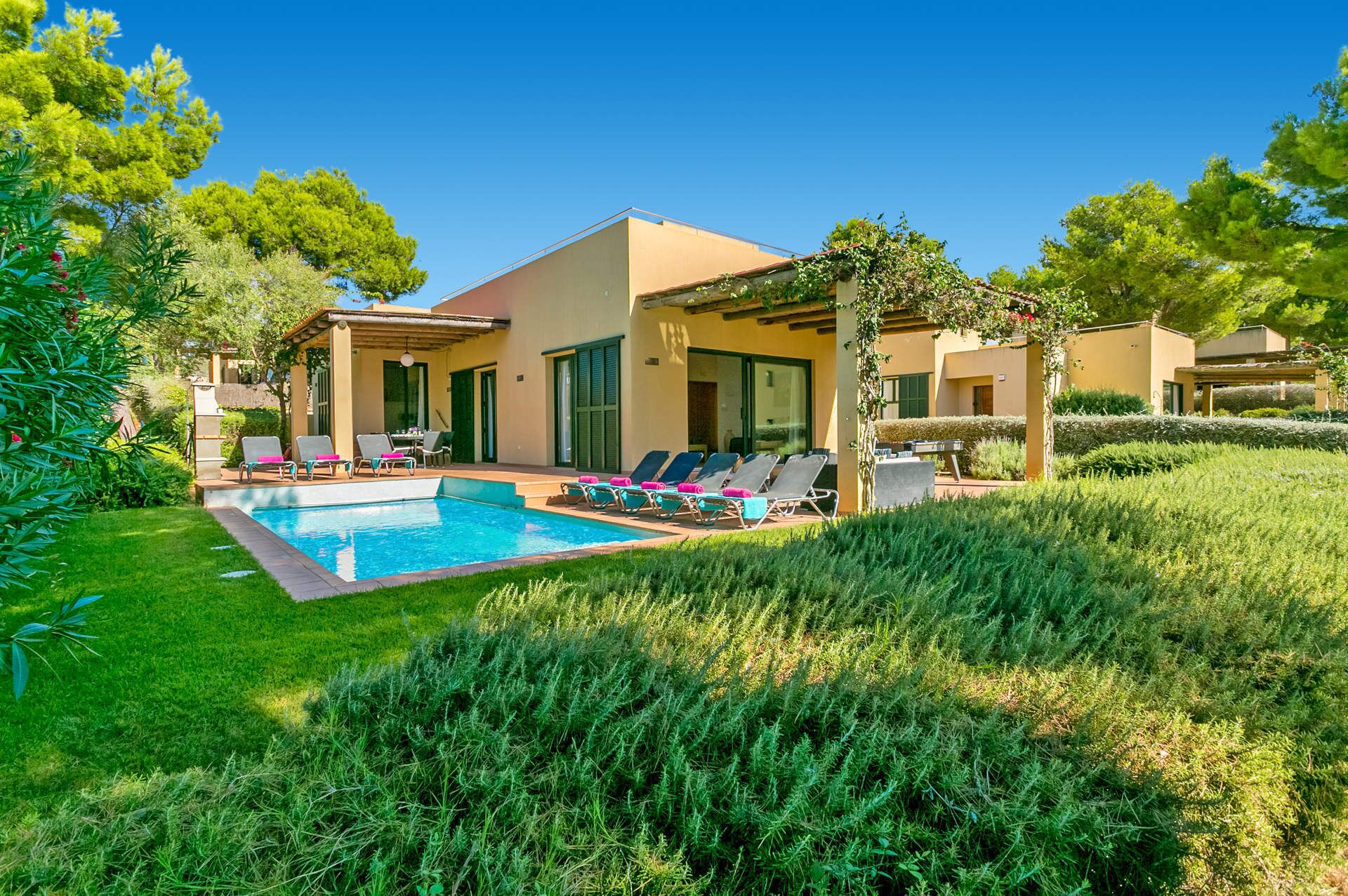 A modern villa with a swimming pool, sun loungers, and a well-maintained garden.