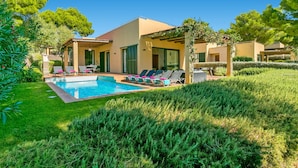 Una villa moderna con piscina, tumbonas y un jardín bien cuidado.