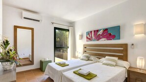 Una camera d'albergo con due letti, un'ampia finestra, un condizionatore, un quadro e un comodino con una lampada.