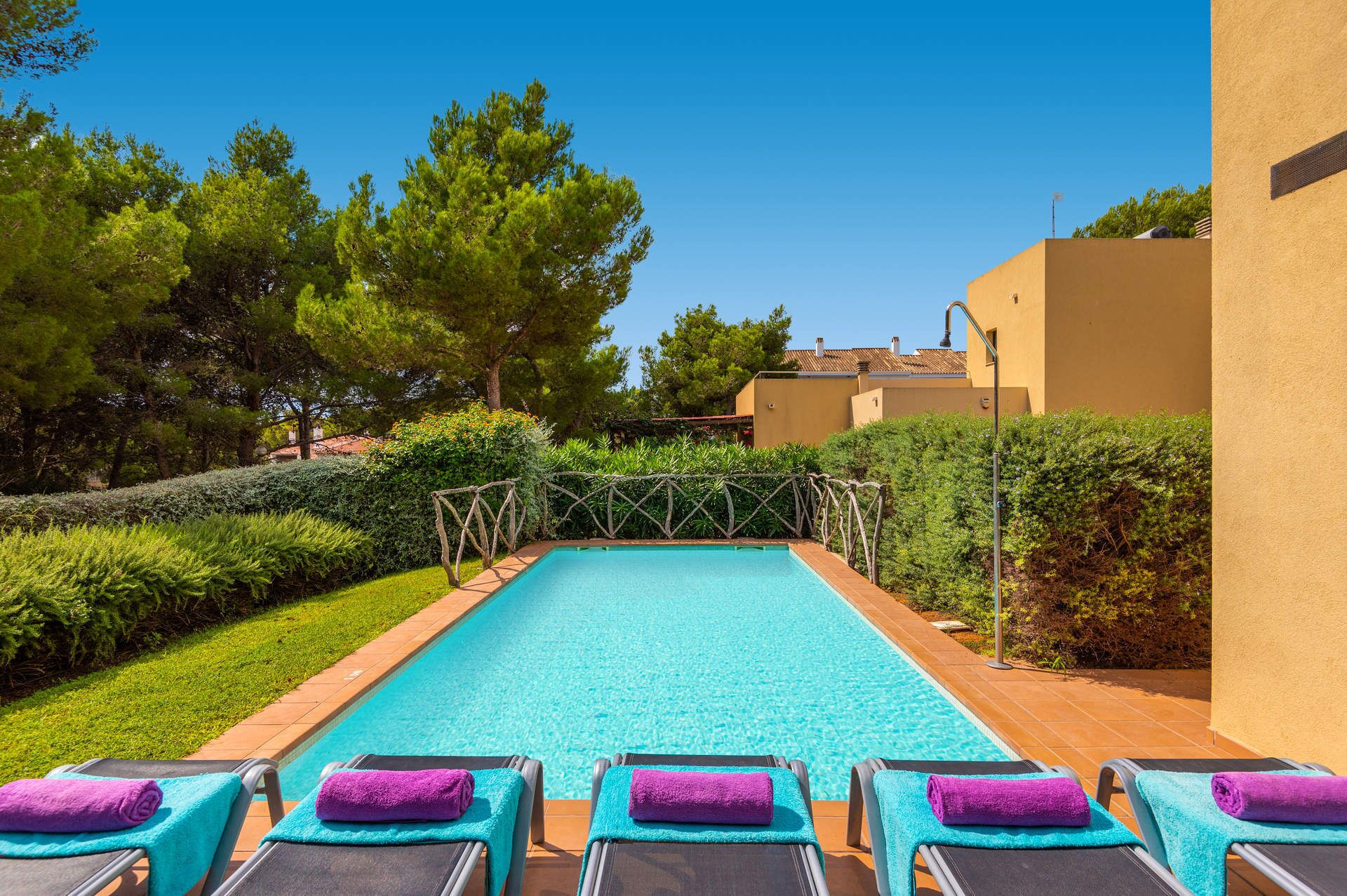 A pool with lounge chairs and towels, surrounded by greenery and buildings.