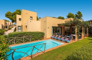 Un espace piscine avec des chaises longues, une pergola et un ciel d’un bleu limpide.