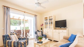 A living room with a sofa, armchair, and a coffee table. There is a television on a cabinet, and a window with curtains. - Villa Las Mariposas by Villa Plus (Es Mercadal)