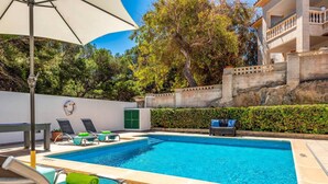 A swimming pool with lounge chairs and a table, surrounded by a low wall and greenery. - Villa Las Mariposas by Villa Plus (Es Mercadal)