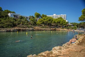 A coastal area with clear water, rocky shore, and buildings in the background. - Villa Maggie by Villa Plus (Ciutadella de Menorca)