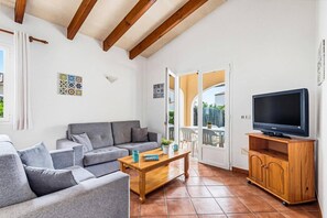 A living room with a grey sofa, a wooden coffee table, a television on a wooden stand, and a balcony with a view.