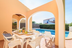 A patio area with a pool, white furniture, and a table set for dining.