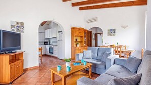 A living room with a sofa, coffee table, TV, and kitchen in the background. - Villa Mango by Villa Plus (Cap d'Artrutx)