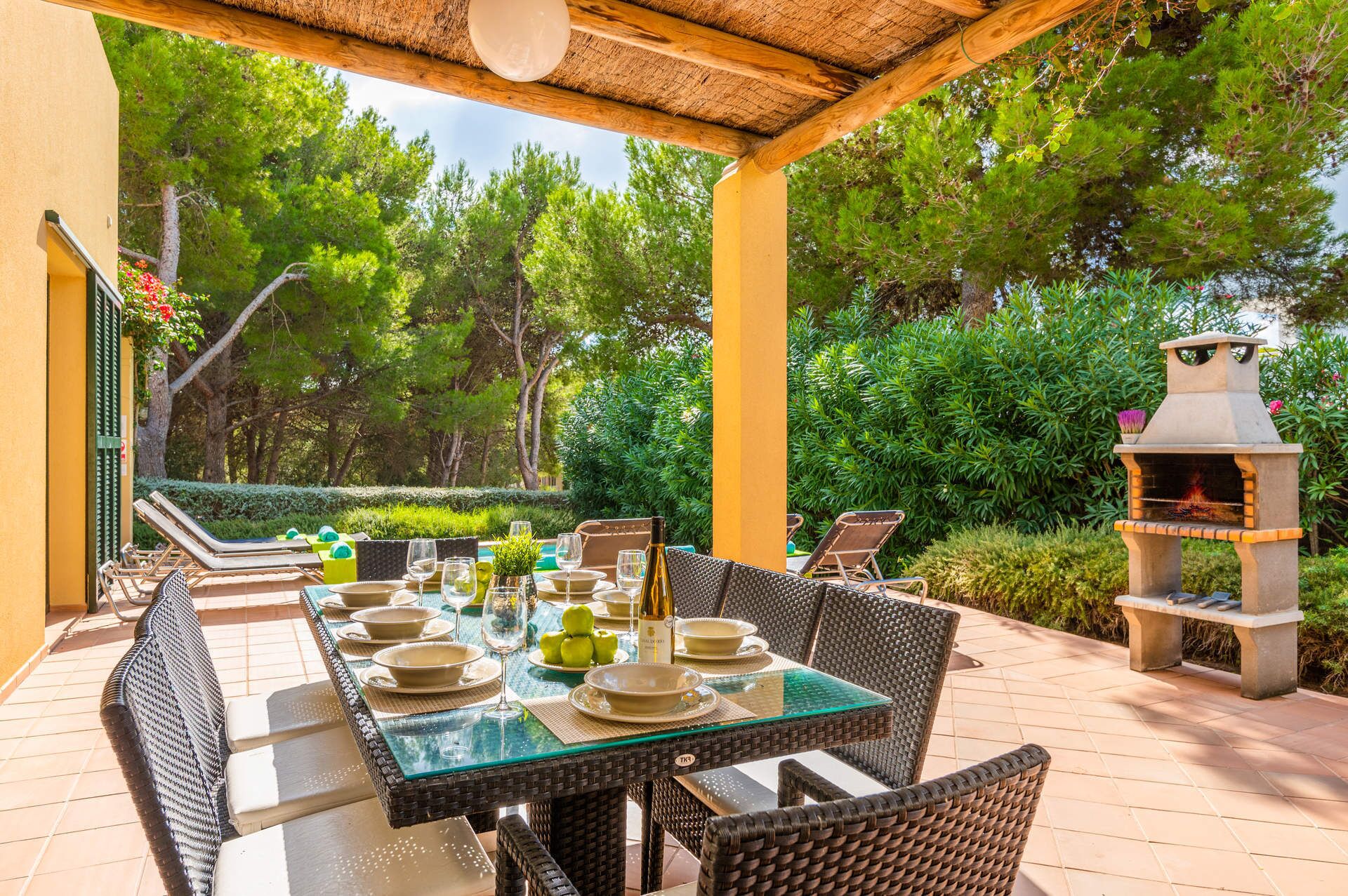 An outdoor dining area with a glass-top table, wicker chairs, and a barbecue grill.