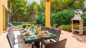 An outdoor dining area with a glass-top table, wicker chairs, and a barbecue grill.