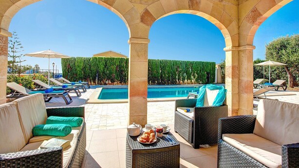 Zona junto a la piscina con sillones de descanso, una mesa con croissants y café, y vista a la piscina.