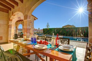 An outdoor dining area with a pool view, stone arches, and a clear sky. - Villa Mares by Villa Plus (Ciutadella de Menorca)