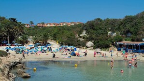 Una playa con sombrillas, gente y un edificio al fondo.