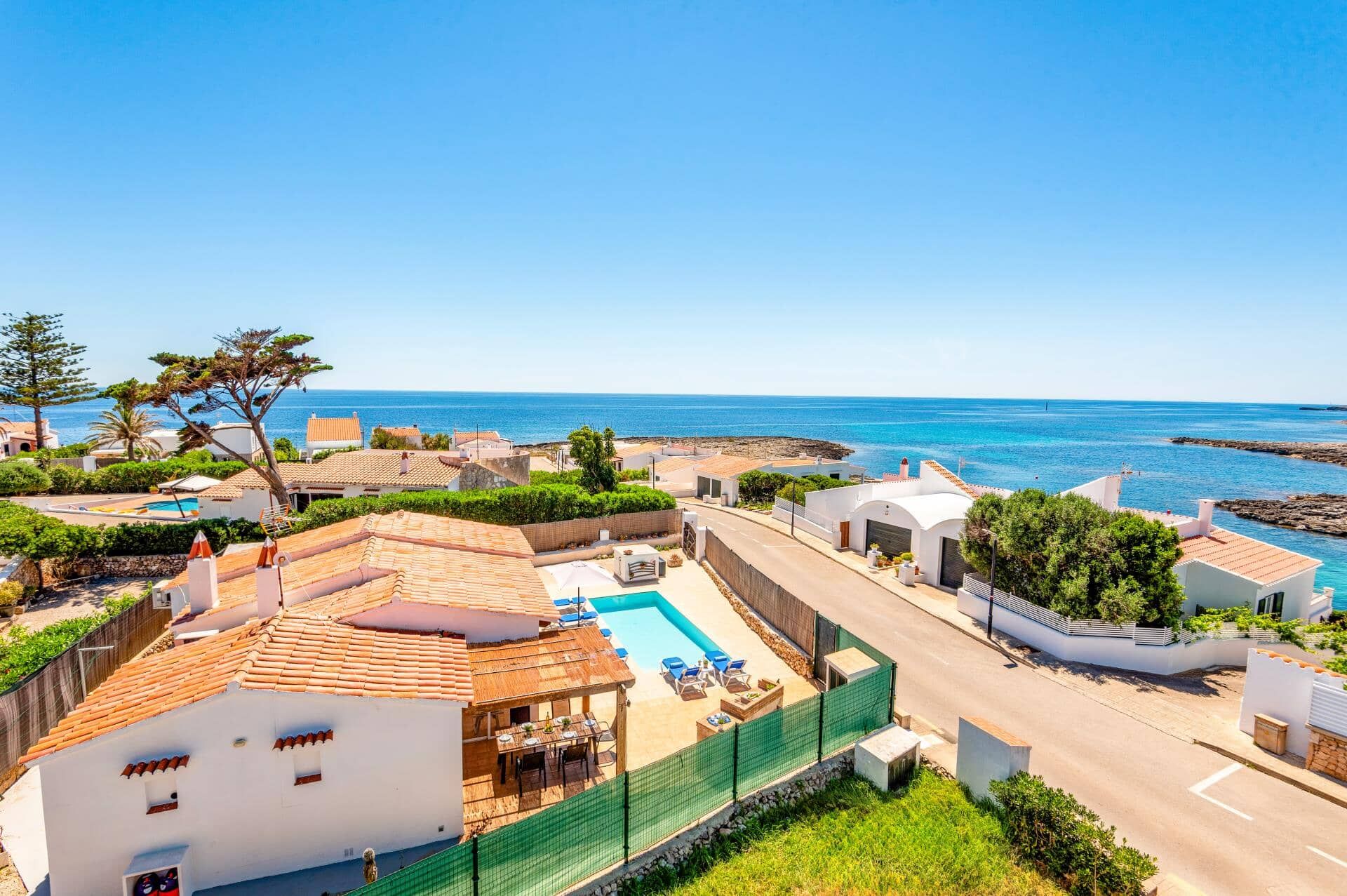 A coastal property with a swimming pool, white buildings, and a view of the sea.