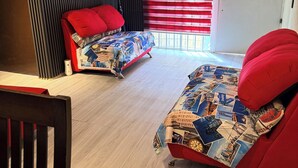 A room with two red beds, a wooden floor, a black acoustic panel, a white door with a window, and a small table.