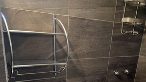 A modern bathroom with a white toilet, dark tiled walls, a shower area, and a towel rack.