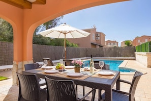 Un espace extérieur aménagé pour les repas, avec des chaises en osier et une table pour deux, donnant sur une piscine.