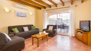 Una sala de estar acogedora con un conjunto de sofá, una mesa de centro, un televisor y un ventanal corredero que da a un espacio al aire libre.