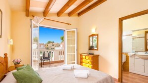 Un dormitorio con cama, cómoda, espejo y balcón con vistas a casas.