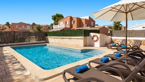 Una piscina con sillas de descanso y una sombrilla, rodeada por un muro de piedra y un seto.