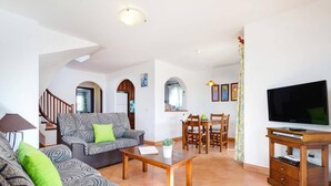 A living room with a sofa, coffee table, TV, and dining area. - Villa Noa by Villa Plus (Cap d'Artrutx)