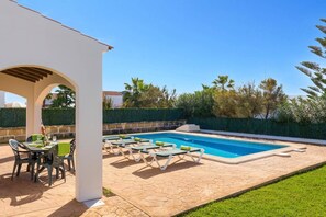A pool area with lounge chairs, a table with a bottle and glasses, and a covered seating area.