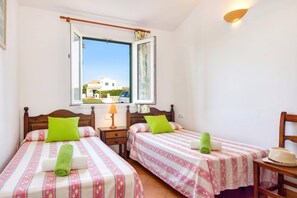 A bedroom with two beds, a window with a view, a bedside lamp, and a chair.