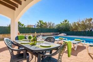 An outdoor dining area with a pool, green chairs, and a table set for two.