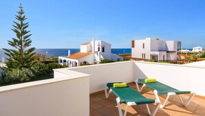 A rooftop terrace with two green lounge chairs, a white building, and a view of the sea. - Villa Noa by Villa Plus (Cap d'Artrutx)