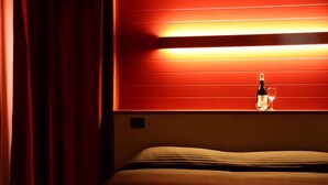 Une chambre d’hôtel avec un lit, un mur rouge et une bouteille de vin posée sur la table de chevet.