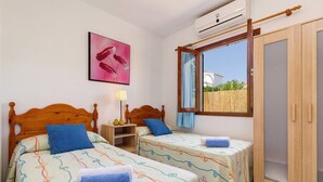 Une chambre à coucher avec deux lits en bois, une fenêtre avec des rideaux, un tableau et un appareil de climatisation.