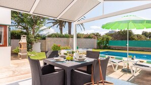 Une terrasse extérieure avec une table dressée pour le repas, une piscine et un parasol vert.