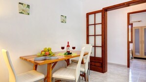 Un coin repas avec une table en bois, deux chaises blanches rembourrées, une bouteille de vin rouge et un verre de vin.