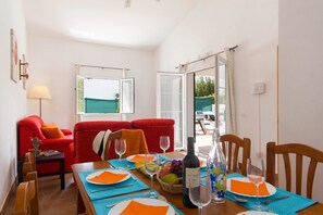 A dining area with a table set for four, a red sofa, and a view of the outdoors through open windows.