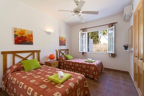 A bedroom with two beds, a ceiling fan, a window with curtains, and a potted plant.
