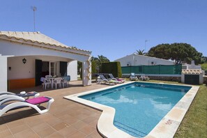 A swimming pool with lounge chairs, a covered seating area, and a building with a tiled roof.