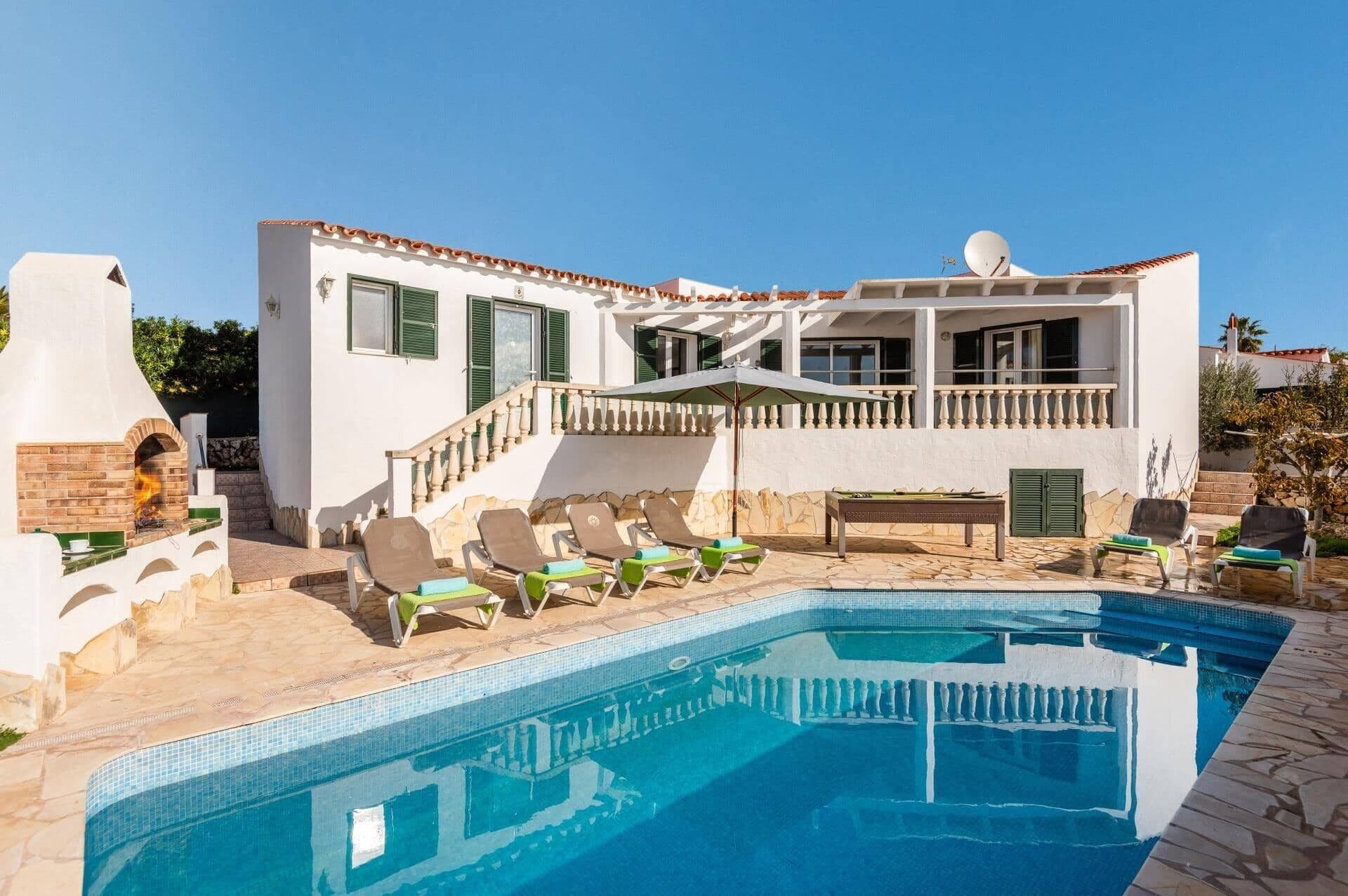 A poolside area with a pool, lounge chairs, and a building with a balcony.