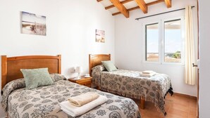 A room with two beds, a window with curtains, and a wooden ceiling. - Villa Santi I by Villa Plus (Cala en Porter)