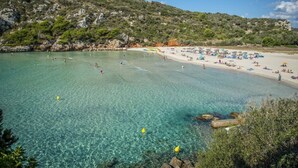 A beach with clear water, a sandy shore, and rocky hills in the background. - Villa Santi I by Villa Plus (Cala en Porter)