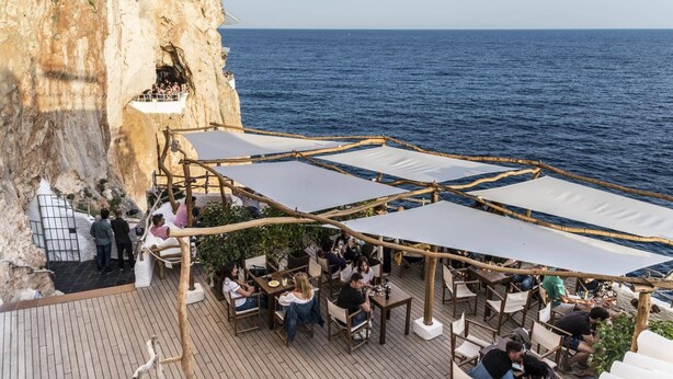 Un restaurante frente al mar con terraza exterior, vistas al océano, un acantilado rocoso y panorama marino.