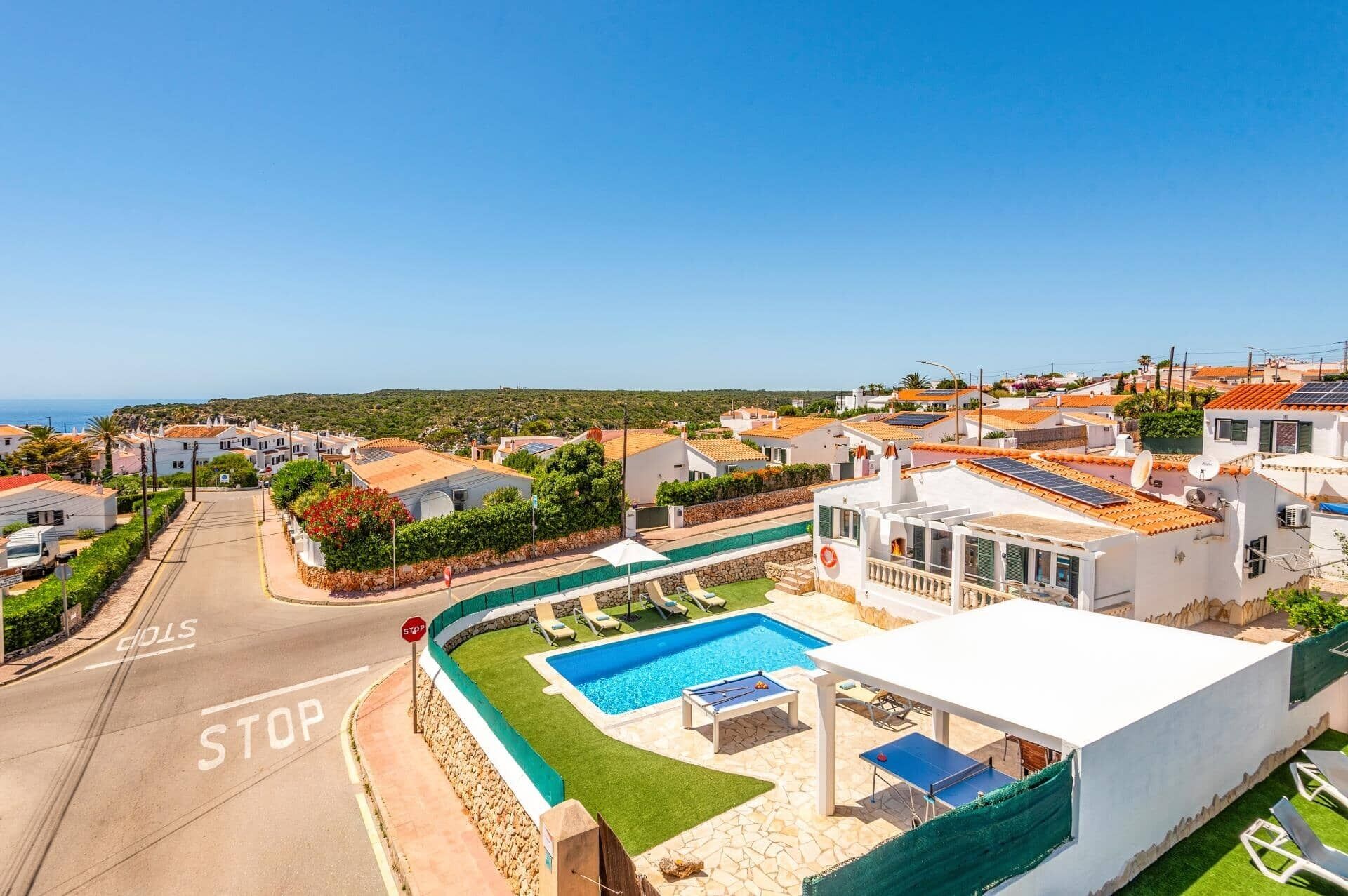 A residential area with a pool, a stop sign, and houses with red-tiled roofs.