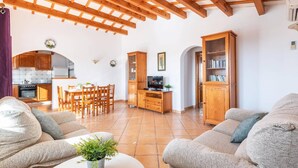 Amplia sala de estar con techo de madera, una mesa de comedor, sofás, un televisor y una estantería.