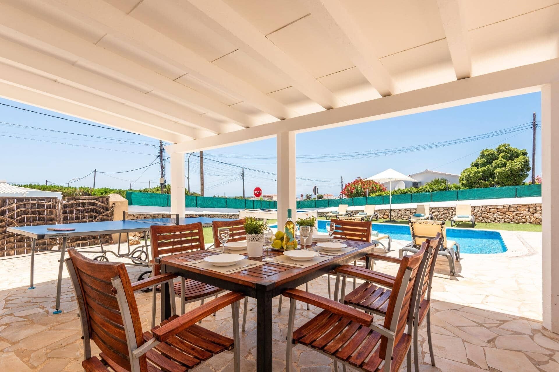 An outdoor patio with a pool, wooden furniture, and a view of the surrounding area.